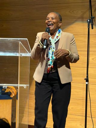Christiane Taubira debout sur scène, un micro à la main, souriante, lors d'un meeting.